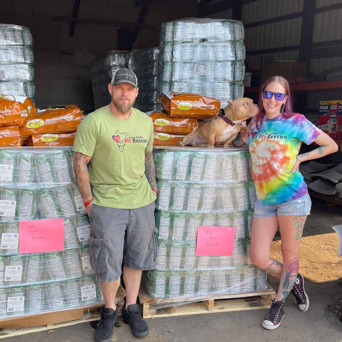 Two Sioux Empire Pit Rescue representatives with a dog beside pallets of donated dog food at Roxi & Co.